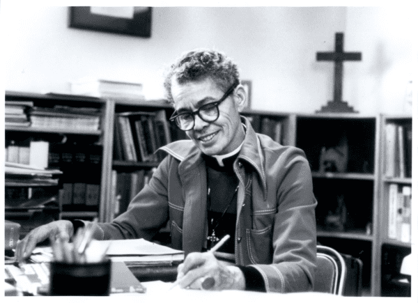 Pauli Murray seated at a desk, writing with a pencil in her left hand