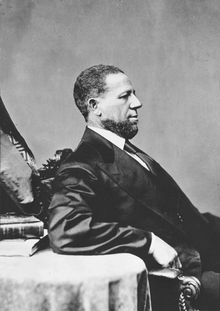 A photo of Hiram Rhodes Revels profile seated in a suit with his arm resting on a table.