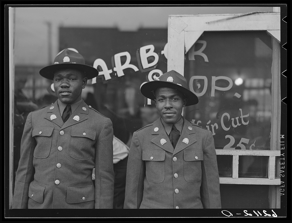 Two Black soldiers posing in front of a barber shop window